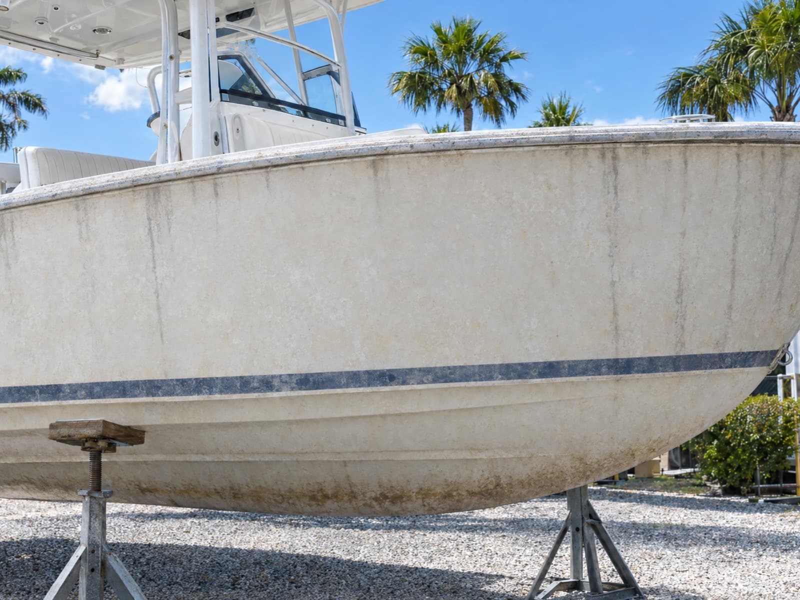 Illustration: the white hull of a center-console boat on stands before a detail, dull and chalky with salt film, waterline scum and dark streaks below the rub rail